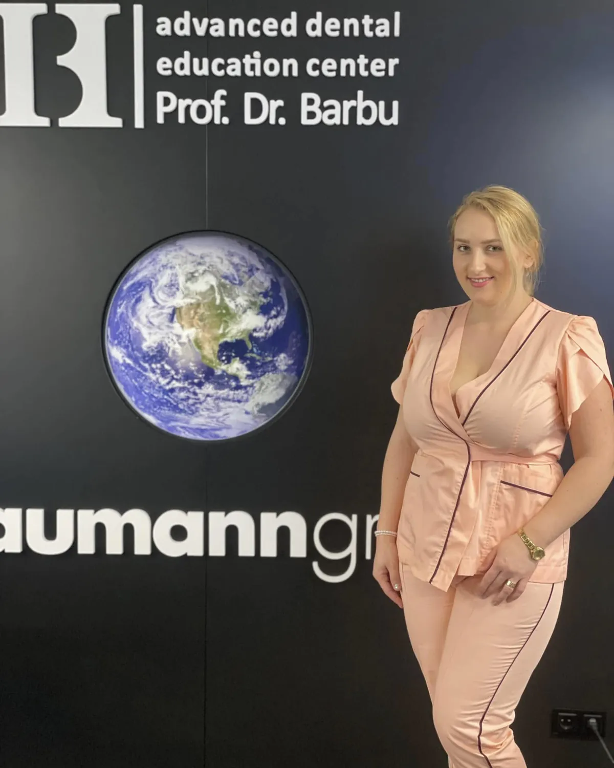 Dr. Ramona Drilea, zâmbind, în costum medical roz, la Prof. Barbu Advanced Dental Education Center